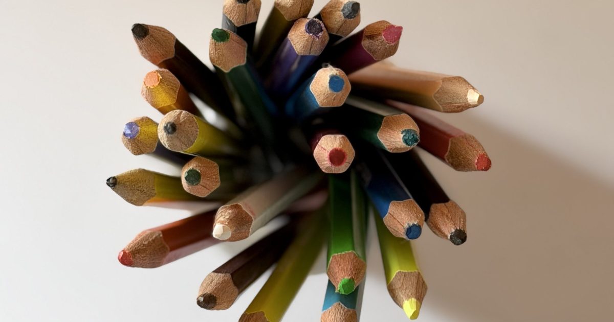 A top-down view of sharpened colored pencils in a radial bundle, forming a bright starburst on a clean white
