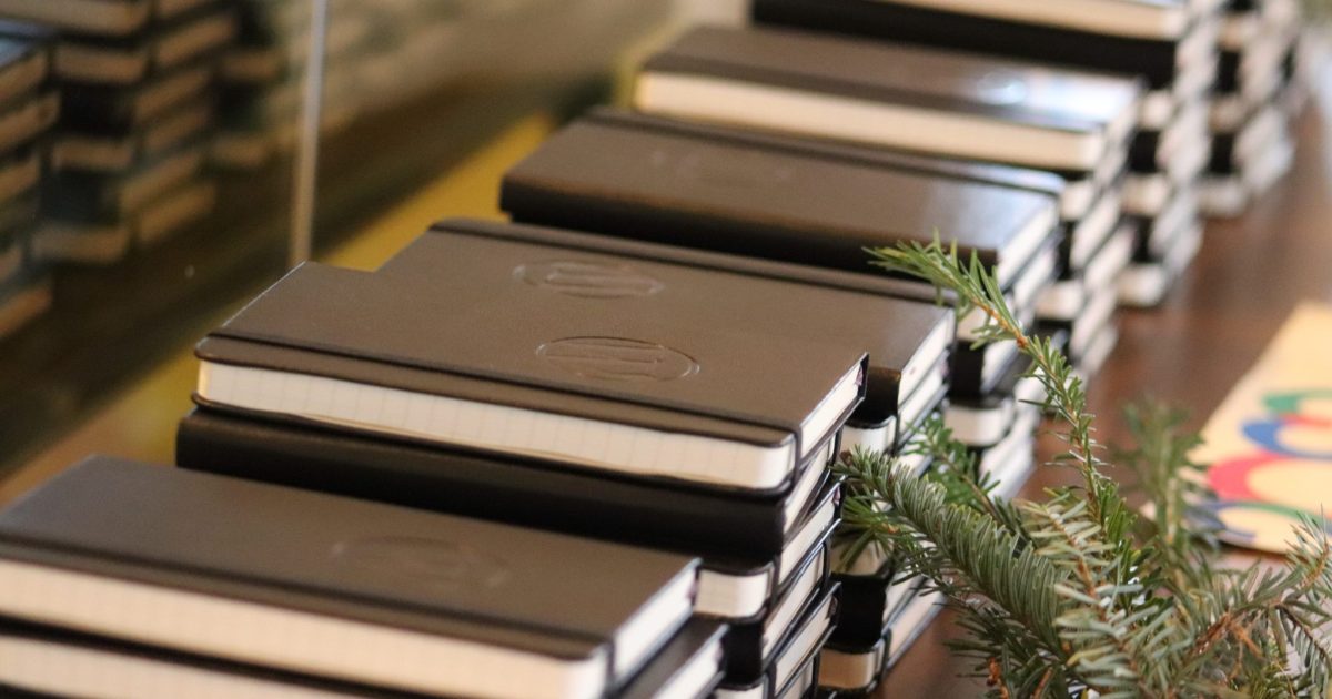 Stacks of black notebooks on a table with evergreen holiday decorations