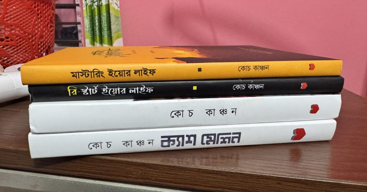 A stack of four Bengali books on a wooden desk, with yellow, black and white covers