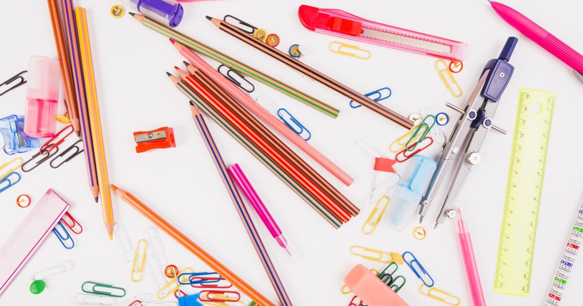 A colorful assortment of stationery items scattered on a white surface, including pencils, pens, paperclips