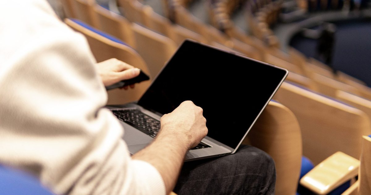 In an empty auditorium, a man sits with a laptop on his lap