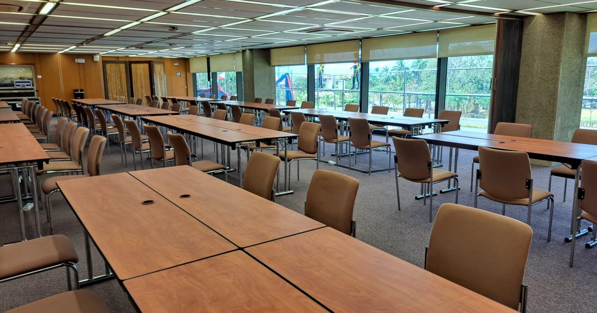 A spacious conference room featuring several rows of rectangular tables arranged for meetings, with beige