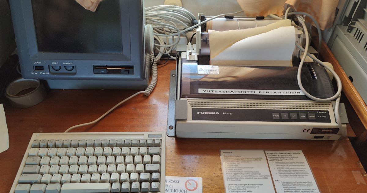 A vintage ship communication setup with a CRT monitor, keyboard, and printer, along with printed