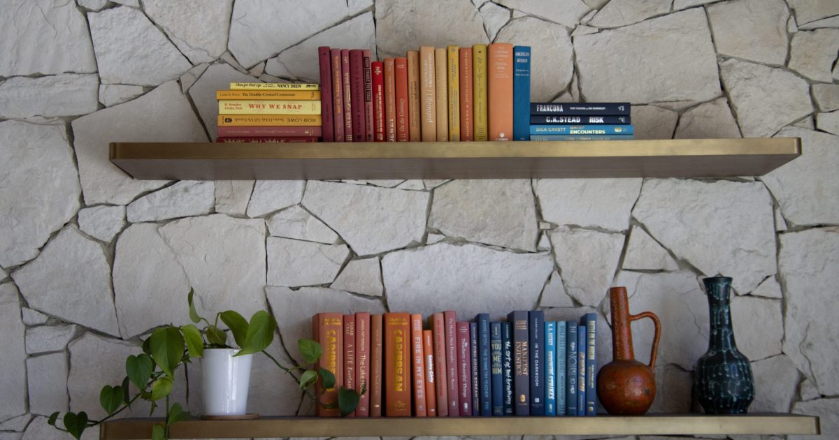 A couple of bookshelves with colorful books on a stone wall