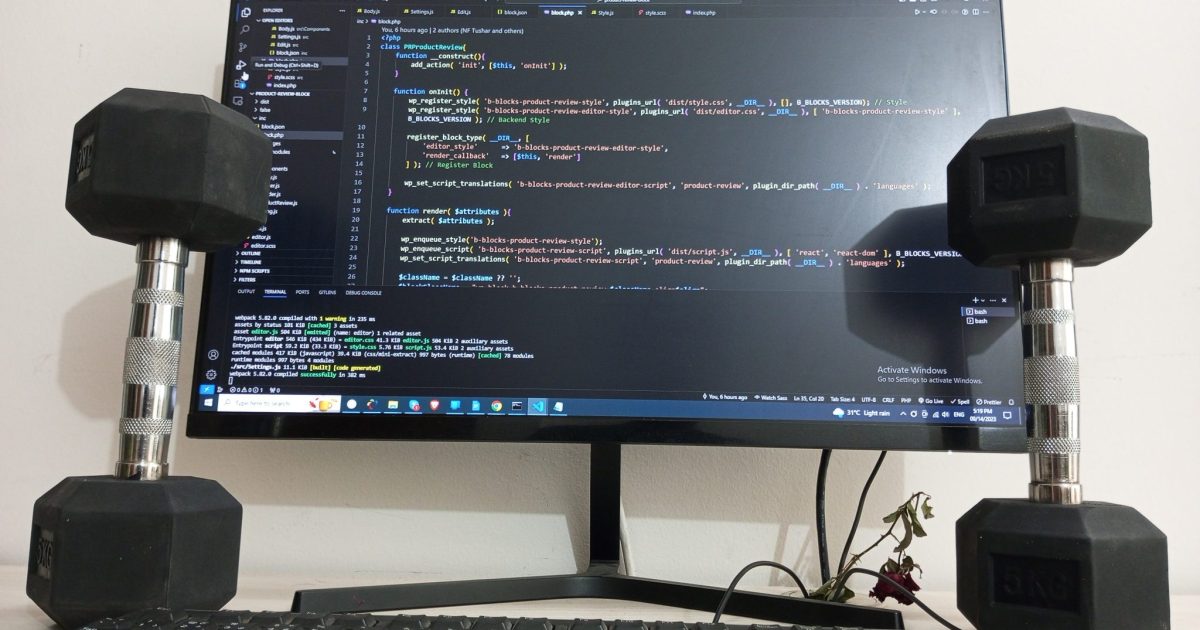 Dumbells rest upright on either side of a keyboard and computer monitor displaying code