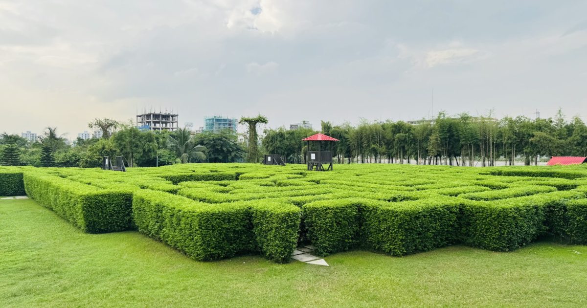 Green hedge maze under a cloudy sky, featuring a small red-roofed lookout tower
