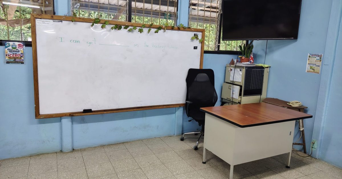 Whiteboard with and english grammar exercise written on it, next to a tracer desk and a tv monitor